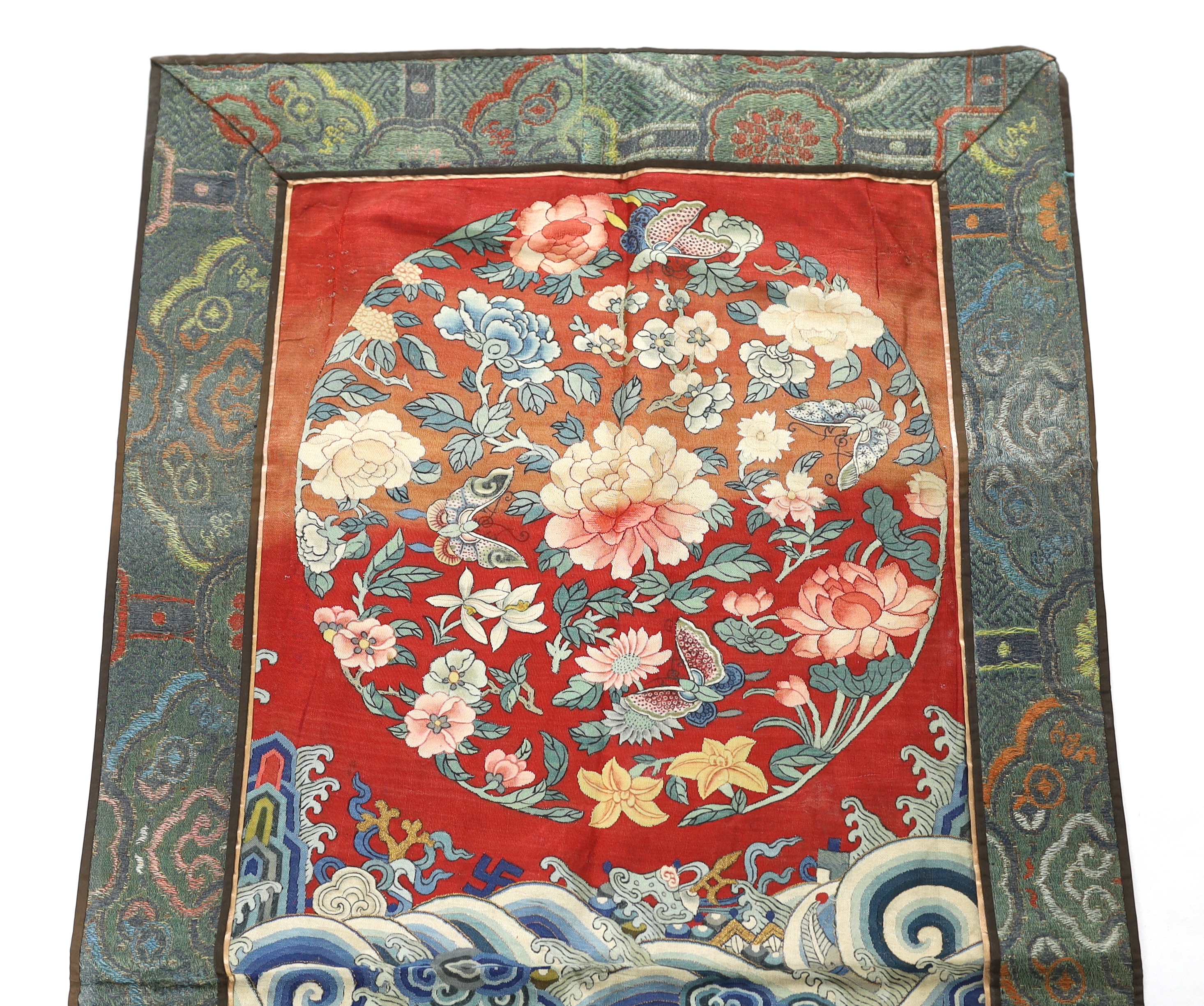 A Chinese Kesi polychrome silk woven panel, Qing dynasty, first half 19th century, possibly the back of a robe, decorated with a roundel of flowers and butterflies above a border of ‘lishui waves’ and auspicious good for